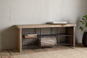 The nkuku Abha Reclaimed Wood & Iron Storage Bench - Natural holds a folded striped blanket and books, set against a pale wall by a potted plant on a woven rug—ideal as an entryway organizer.
