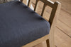 Close-up of the nkuku Avanthi Upholstered Sleigh Bench in charcoal, featuring a carved wooden frame and dark gray upholstery, placed on a wooden floor.