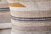 Close-up of the nkuku Aravali Wool Cushion Cover - Ochre, featuring a textured woven design with beige, cream, brown, black stripes, and a mustard yellow triangle. A similar cushion is partially visible beside it.
