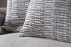 Close-up of two nkuku Aahna Wool Cushion Covers in charcoal, featuring a woven design, displayed on a beige sofa next to a knitted blanket.
