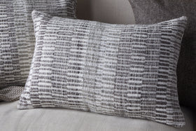 The nkuku Aahna Wool Cushion Cover in Charcoal features a textured, woven design in gray and white wool and recycled polyester, styled here on a light fabric sofa with coordinating cushions in the background.