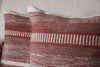 Two Aakash Wool Cushion Covers in earthy rust tones by nkuku, featuring textured horizontal and vertical woven stripes, add warmth and charm as decorative pillows on a light-colored sofa.