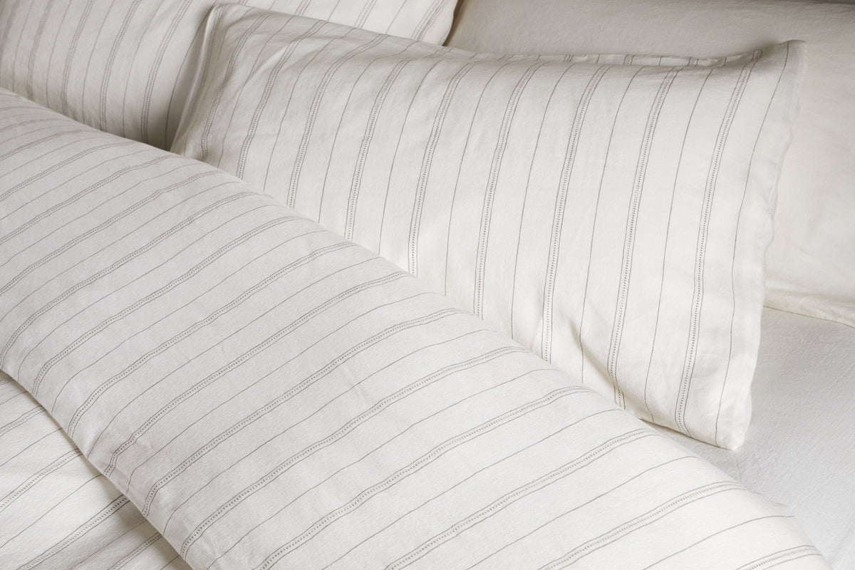 Close-up of a neatly made bed with the nkuku Anta Hemp & Cotton Duvet Cover in sage green, paired with matching pillow and sheet for a fresh, airy look. Bedding features breathable hemp-cotton blend for comfort and style.