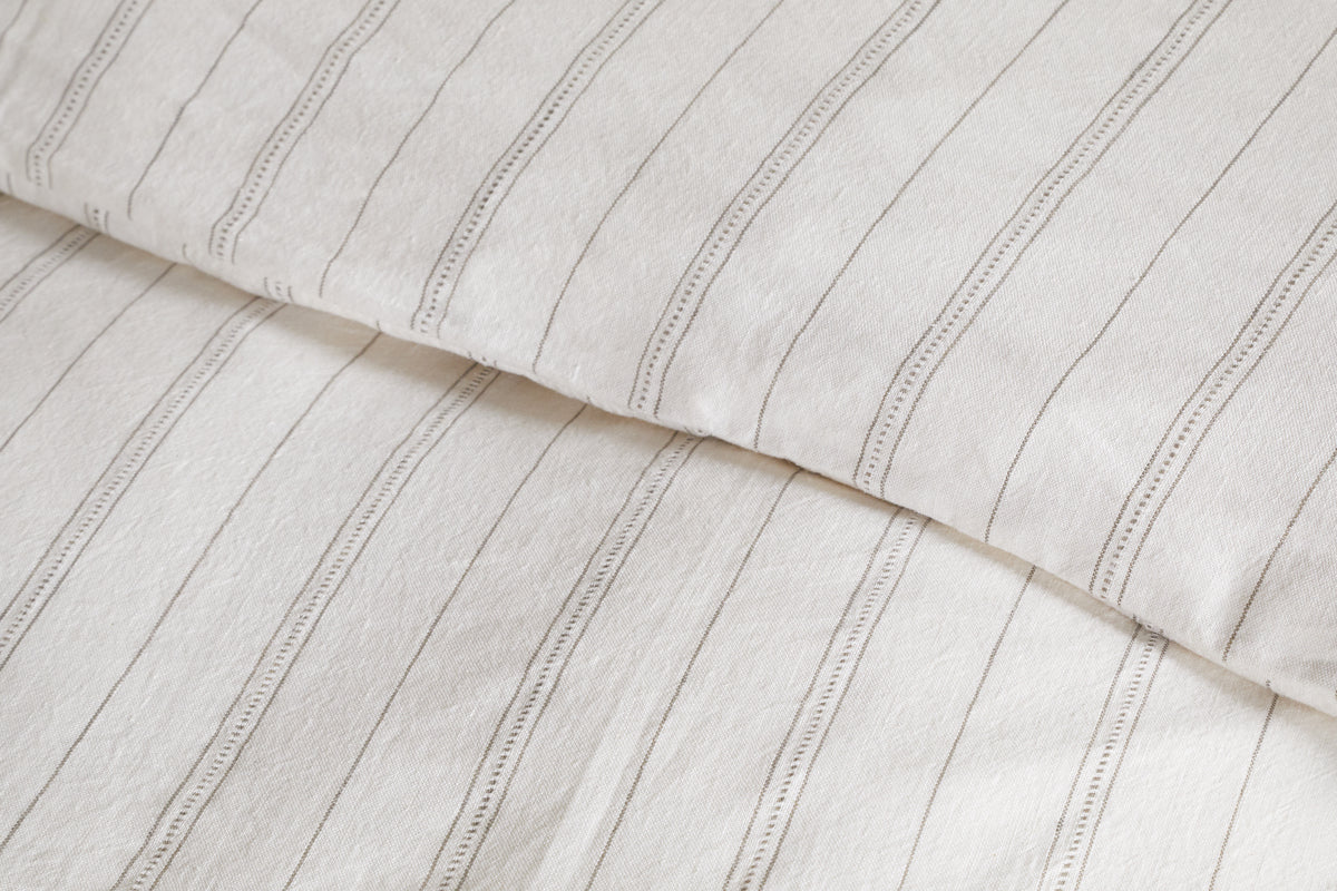 Close-up of breathable bedding with thin, vertical black stripes and a slightly wrinkled texture. Pictured is a pillow and the Anta Hemp & Cotton Duvet Cover in soothing sage green by nkuku.