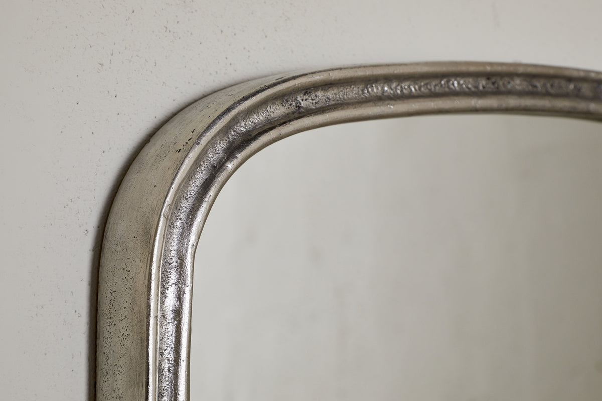 Close-up of the top left corner of the nkuku Almora Wall Mirror - Antique Nickel, featuring a textured metallic aluminium frame against a light-colored wall.
