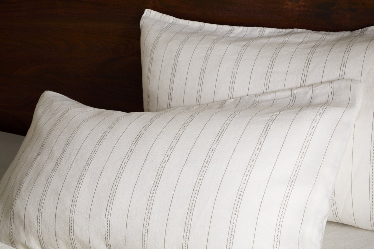Two pillows in nkukus Anta Hemp & Cotton Housewife Pillowcases in sage green are neatly arranged against a dark wooden headboard, with one pillow slightly overlapping the other.