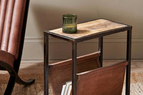 The nkuku Alera Side Table features a rustic leather base, mango wood top, and sturdy iron frame. It’s perfect for holding a green glass above and includes space below for storing magazines in style.