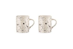 Two nkuku Ama Mug - Tall ceramic mugs feature a white base with a black splatter finish and handles. Each artisan mug displays a minimalist face—two black dots for eyes and a short black line for the mouth.