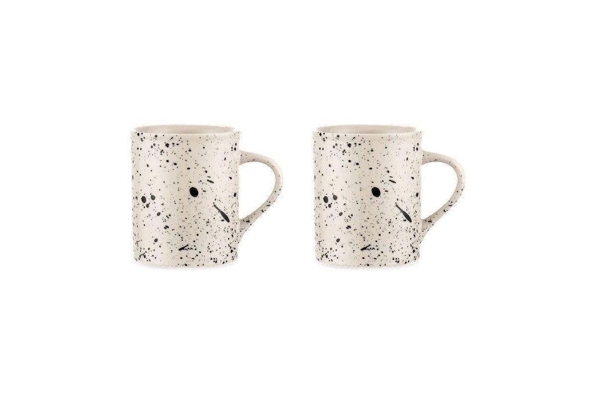 Two nkuku Ama Mug - Tall ceramic mugs feature a white base with a black splatter finish and handles. Each artisan mug displays a minimalist face—two black dots for eyes and a short black line for the mouth.