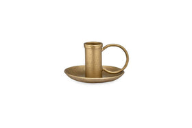 The Amri Iron Candlestick by nkuku features an antique brass finish, a round base, a short holder for dinner candles, and a large circular side handle—all displayed on a plain white background.