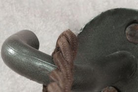 Close-up of the nkuku Aniko Iron Hook (Set of 2) mounted on a surface with two rusted screws, holding a thick brown rope. The light, textured background highlights the details of both the rope and the hook.