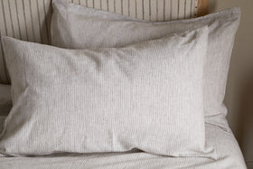 Two espresso-toned Borba Hemp & Cotton Housewife Pillowcases from nkuku rest against a matching headboard and bedsheet, creating a coordinated and minimalist bedroom look.