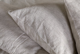 A close-up of the nkuku Borba Hemp & Cotton Housewife Pillowcases in Espresso, featuring soft, slightly wrinkled fabric with subtle stripes, resting on a matching bedsheet for a cozy and inviting look.