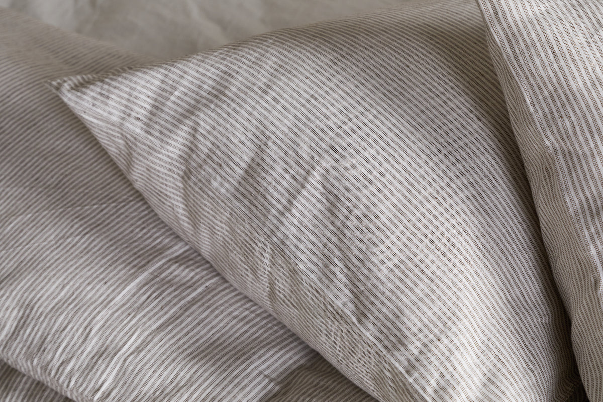 A close-up of the nkuku Borba Hemp & Cotton Housewife Pillowcases in Espresso, featuring soft, slightly wrinkled fabric with subtle stripes, resting on a matching bedsheet for a cozy and inviting look.