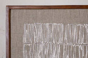 The Birala Hand Stitched Wall Art - Natural by nkuku displays irregular vertical white threads on beige fabric, framed in sustainable mango wood, highlighting the textured abstract pattern against a softly textured wall.