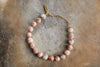 The Cerita Bracelet - Rhodochrosite by nkuku features round marbled pink and white semi-precious stones, gold spacer beads, and a gold chain clasp—an elegant accessory for any occasion.