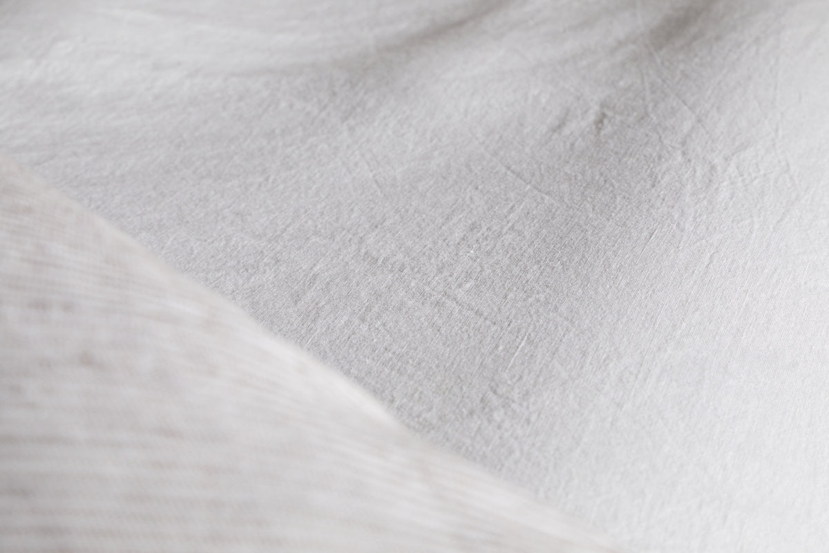 Close-up of nkukus Cela Hemp & Cotton Fitted Sheet in Natural, highlighting its white, textured surface with visible fibers and gentle folds for a soft, breathable bedding look.