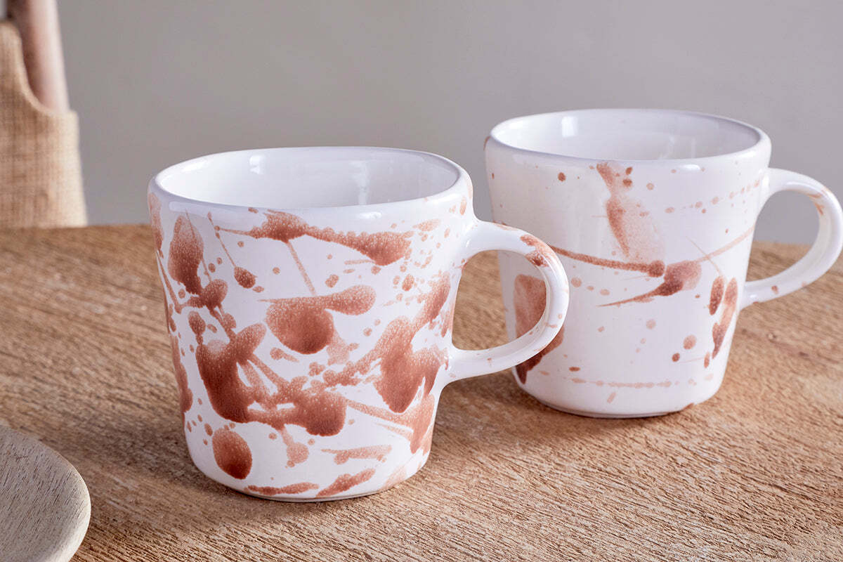 The nkuku Canela Mug set in Dusty Terracotta features two ceramic mugs with brown abstract splatter designs, offering a cozy, minimalist touch to your space. Perfect for enjoying beverages together or as a stylish gift.