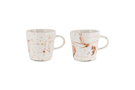 The nkuku Canela Mug - Dusty Terracotta (Set of 2) features two ceramic mugs with handles, each showcasing a unique brown splatter pattern for an artisanal look. The mugs are displayed against a plain white background.