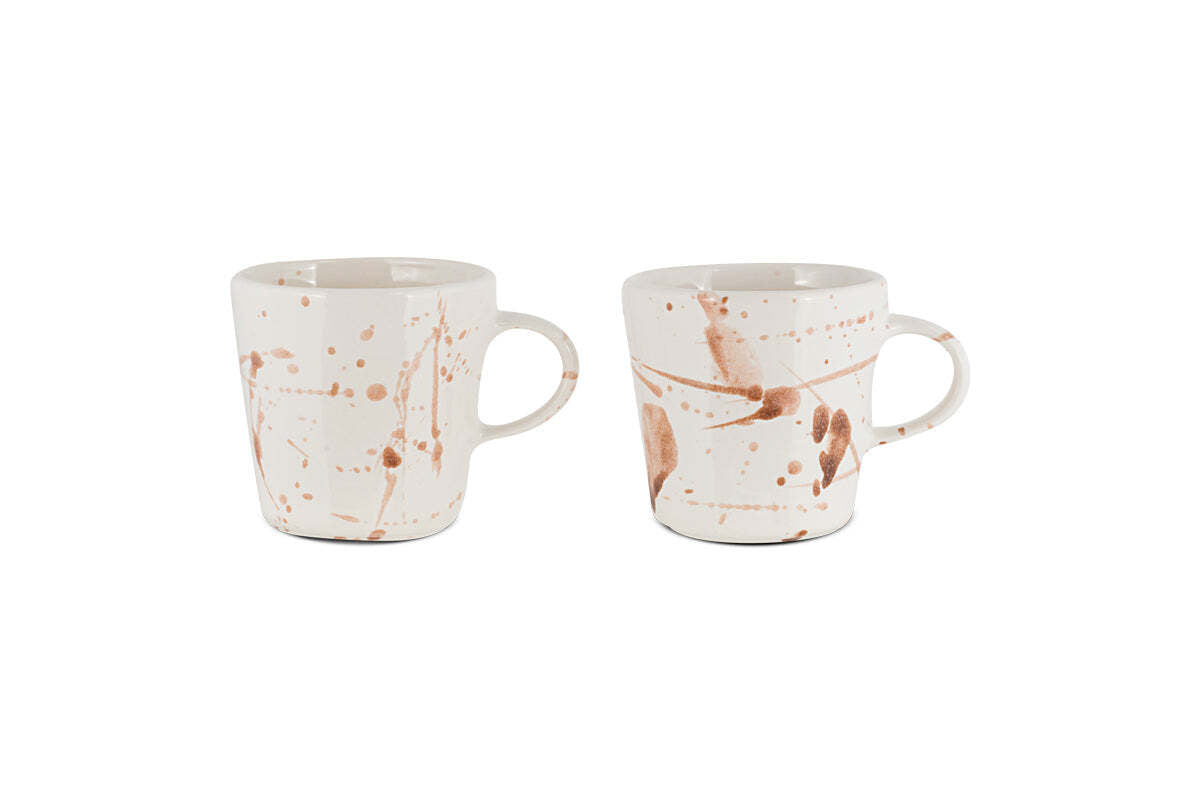 The nkuku Canela Mug - Dusty Terracotta (Set of 2) features two ceramic mugs with handles, each showcasing a unique brown splatter pattern for an artisanal look. The mugs are displayed against a plain white background.