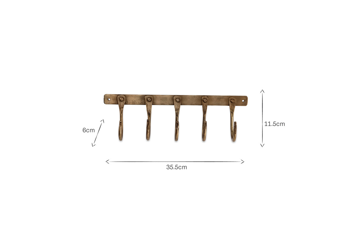 The nkuku Kuna Iron Hooks - Antique Brass features five antique brass-finished hooks on a rectangular plate, ideal for small storage. The rack measures 35.5cm wide by 8cm high; each hook is 11.5cm long.