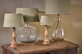 Four nkuku Dia Jute Lampshade - Natural table lamps sit on a rustic wooden surface. Two have clear glass bases (round and teardrop); two feature light wood bases. Visible cords add charm, making them ideal for ambient lighting.