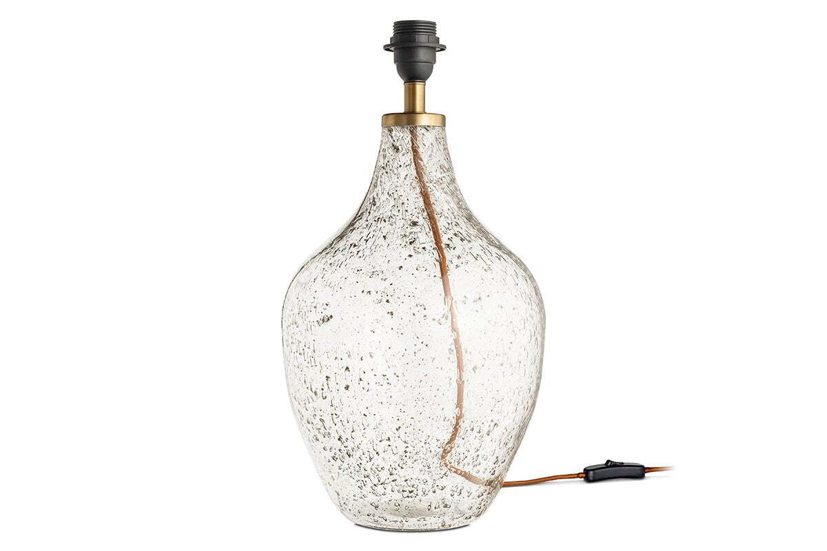 The Damini Recycled Glass Table Lamp by nkuku features a clear, bulbous base with a bubbled texture, brass neck, black socket, and visible cord. Crafted from recycled glass. Lampshade not included.