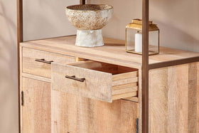 The nkuku Dasai Mango Wood Storage Unit features two doors and two drawers, one partially open. A speckled ceramic bowl and gold lantern with a white candle rest on top—stylish storage for your living room against a beige wall.