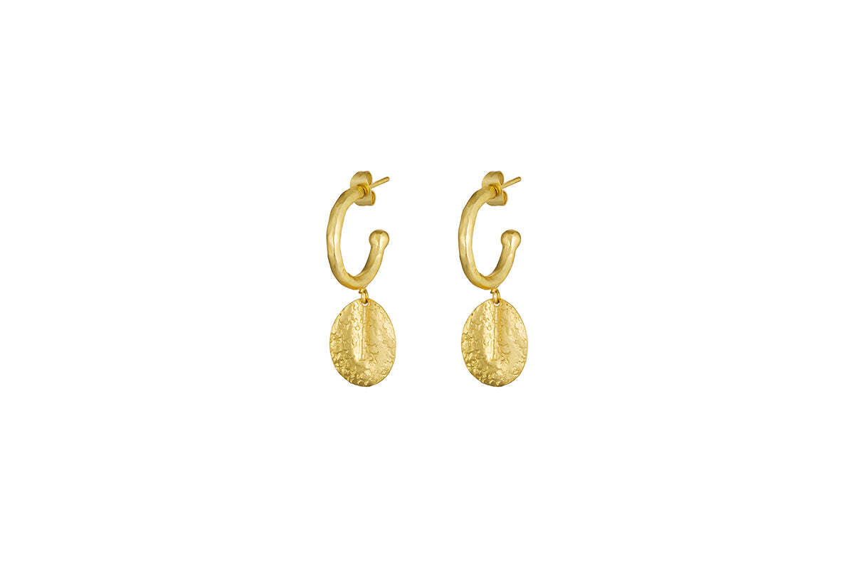 The Esta Hoop Earrings - Gold by nkuku feature textured, hammered oval pendants hanging from each shiny hoop, offering a simple and elegant handcrafted style. Shown in one size against a plain white background.