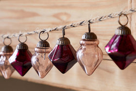The Ekiti Bauble Garland - Ruby & Copper by nkuku features vintage-style recycled glass ornaments in deep red and copper, each with unique geometric shapes, hanging from twine—a perfect accent for classic vintage decor.