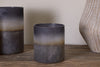 The nkuku Etti Tealight Holders in Navy & Smoke, featuring a small cylindrical matte ceramic design with a dark gradient and rustic finish, sit on a wooden surface, alongside a matching larger holder and textured vase in the background.