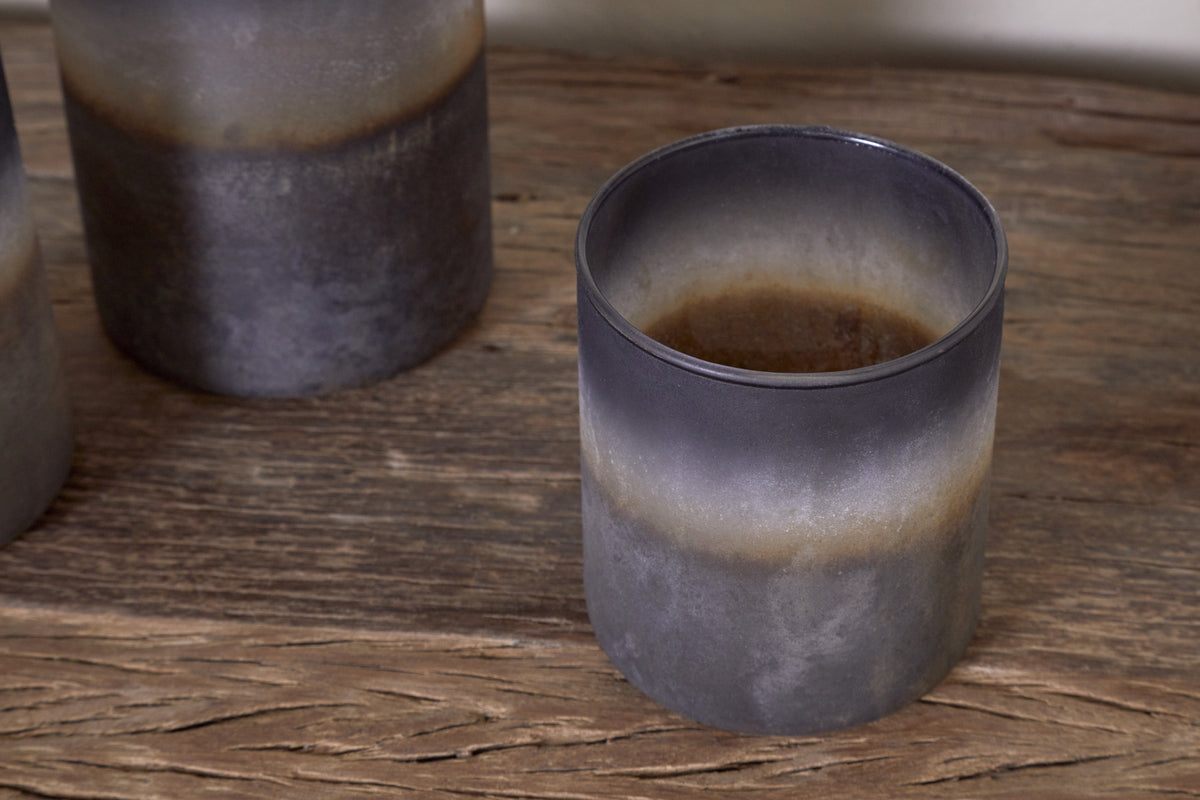 A close-up of nkukus Etti Tealight Holders in navy and smoke, featuring a rustic matte finish, captures their cozy charm on a wooden surface.