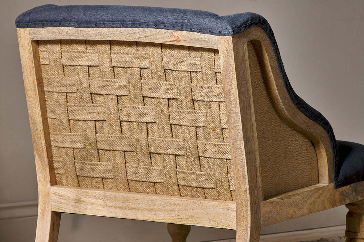 A close-up of the Elbu Deconstructed Linen Armchair by nkuku highlights its light mango wood, exposed woven burlap back, and charcoal linen fabric along the edges and seat—showcasing rustic charm with a modern twist.