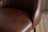 Close-up of the nkuku Harsha Leather Counter Chair in chocolate brown, featuring stitched backrest detailing and a smooth seat—ideal for kitchen island seating—with a wooden floor backdrop.