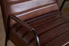 Close-up of the nkuku Hadithi Leather Occasional Chair in chocolate brown buffalo leather, featuring a ribbed seat and back, black metal armrests, and set on a wooden floor.