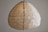 The nkuku Hirana Cotton Lampshade - Natural - Large features a teardrop shape with textured off-white cotton, visible seams, and a slightly wrinkled look, making it a stylish accent for bedrooms when hung from a black pendant fitting against any plain wall.