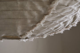 Close-up of the Hirana Cotton Lampshade by nkuku in natural, large size: off-white textured cotton with frayed edges and visible stitching, softly draped—perfect for adding warmth to any bedroom or living space.