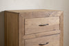 Close-up of the upper section of the nkuku Iya Reclaimed Wood Chest of Drawers - Natural - Small, showing two drawers with simple metal handles against a textured light wall.