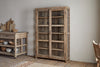 The Ibo Reclaimed Wood & Glass Cabinet - Natural - Wide by nkuku features classic wooden construction, glass panel doors, and antique brass handles for a rustic yet elegant look.