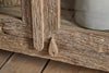 Close-up of the nkuku Ibo Reclaimed Wood & Glass Cabinet - Natural - Wide, highlighting its rustic door with a drop-shaped wooden knob and textured weathered wood grain; a ceramic vase appears to the right.