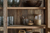 The nkuku Ibo Reclaimed Wood & Glass Cabinet - Natural - Wide showcases glassware, a wooden bowl, pasta and brown sugar in cork-lidded jars, and a glass jar with honey dipper, all beautifully set against rustic wood and glass panels.