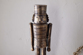 The Imay Nutcracker - Antique Brass by nkuku features a wooden soldier with a cylindrical hat, round eyes, and a mustache in a detailed uniform—ideal for festive styling or as part of your decorative nutcracker display.