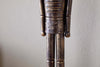 A close-up of the Imay Nutcracker - Antique Brass by nkuku shows its textured dark brown and gold finish, stylized cylindrical arms, and decorative waist carvings—perfect for festive or seasonal displays.