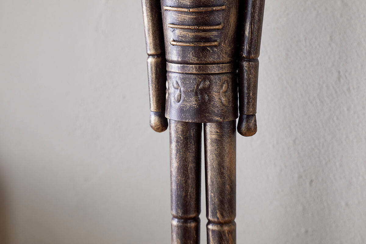A close-up of the Imay Nutcracker - Antique Brass by nkuku shows its textured dark brown and gold finish, stylized cylindrical arms, and decorative waist carvings—perfect for festive or seasonal displays.