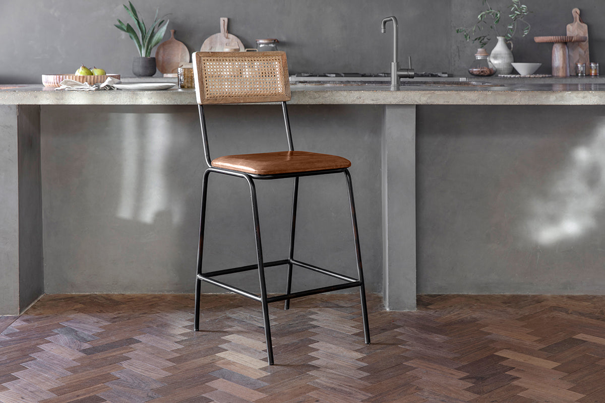 The Iswa Leather & Cane Counter Chair by nkuku in aged tan brings charm and comfort to your kitchen island with its classic cane back and elegant design.
