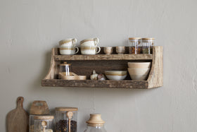 The nkuku Ibo Reclaimed Wood Storage Shelf in Natural hangs on a light wall, displaying ceramic cups, bowls, and spice jars above, with weathered wooden shelves below for extra kitchen storage of glass jars and a cutting board.