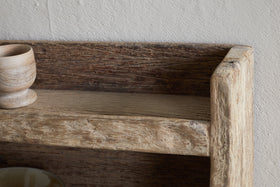 Close-up of the nkuku Ibo Reclaimed Wood Storage Shelf - Natural, highlighting its weathered wood texture, with a small wooden cup on the left. This rustic wall-hung shelf adds charming kitchen storage against a light textured wall.