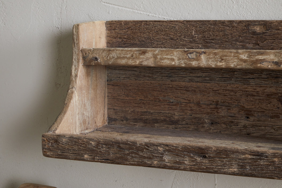 A close-up of the nkuku Ibo Reclaimed Wood Storage Shelf - Natural, wall-mounted on a light textured surface. Made from weathered wood with visible grain and knots, it offers simple, hand-crafted style perfect for kitchen storage.