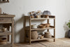 The nkuku Ibo Reclaimed Wood Pantry Standing Shelves in Natural showcase woven baskets, ceramic dishes, and glass containers in a neutral kitchen with a light textured wall and wooden floor.