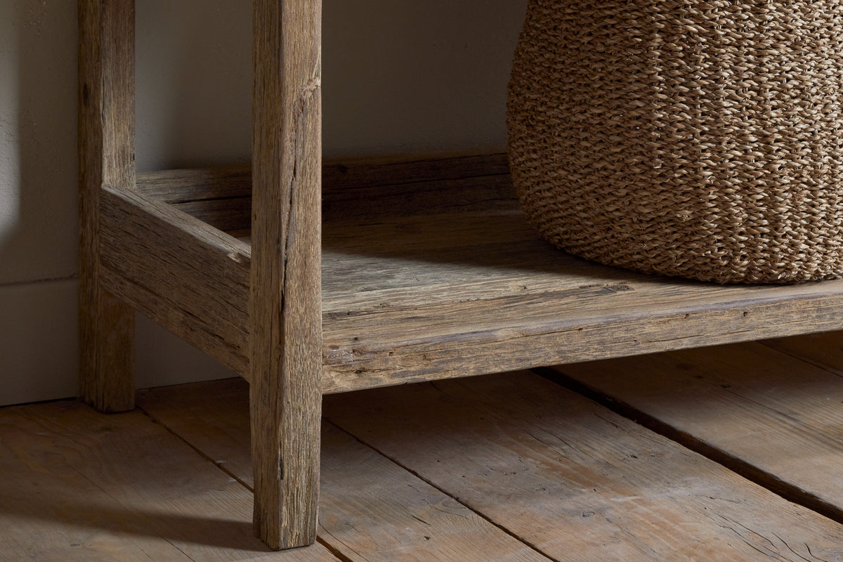 A close-up of the nkuku Ibo Reclaimed Wood Pantry Standing Shelves - Natural, featuring open shelving on a wooden floor with a woven basket on the lower shelf, showcasing its rustic wood grain and texture.